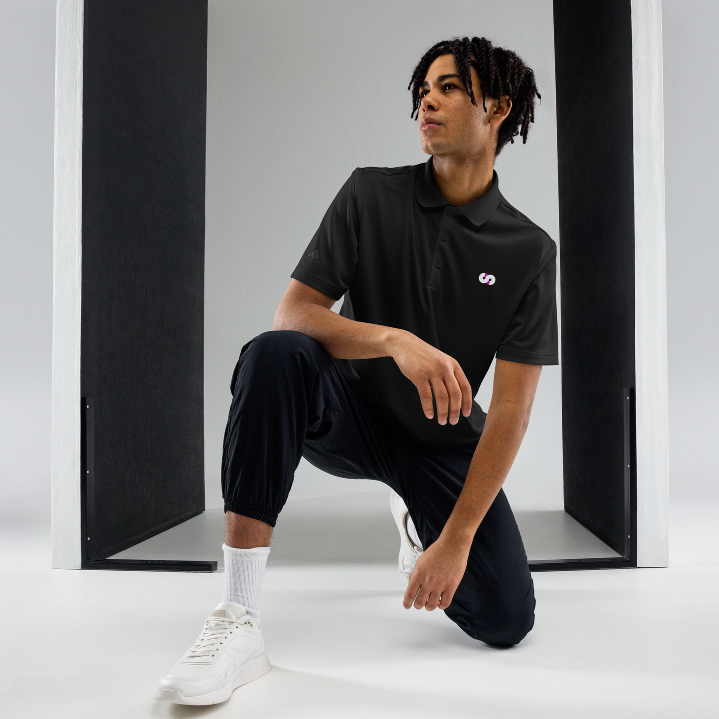 Persona en posición de rodillas con Polo Negro VOOM x adidas — The Discipline Code en espacio minimalista y ropa deportiva.