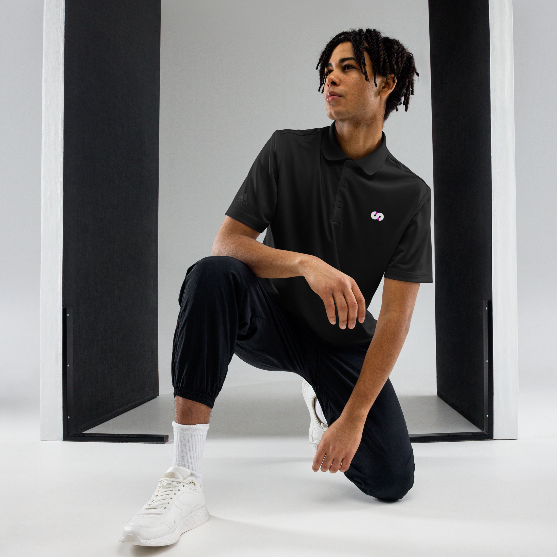 Persona en posición de rodillas con Polo Negro VOOM x adidas — The Discipline Code en espacio minimalista y ropa deportiva.