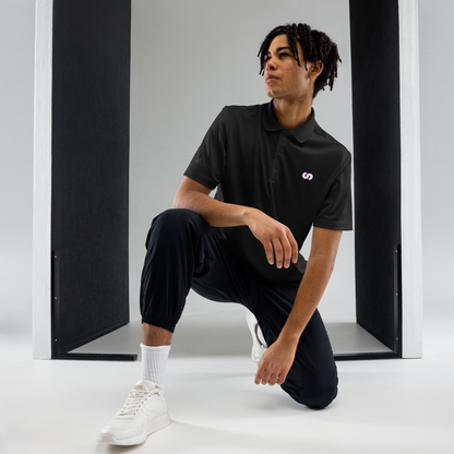 Persona en posición de rodillas con Polo Negro VOOM x adidas — The Discipline Code en espacio minimalista y ropa deportiva.