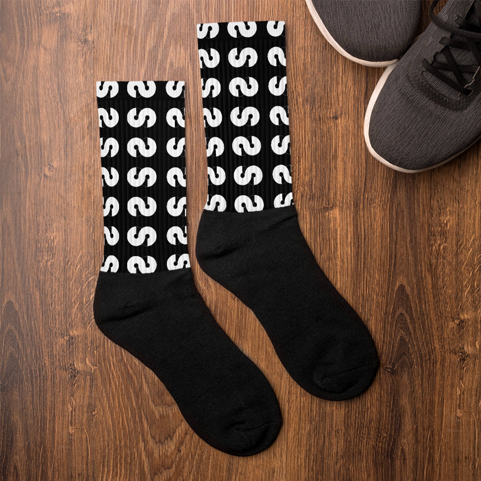 Calcetines VOOM — The Ground Signal largos con diseño de patrón blanco repetido sobre fondo negro sobre piso de madera junto a zapatillas.