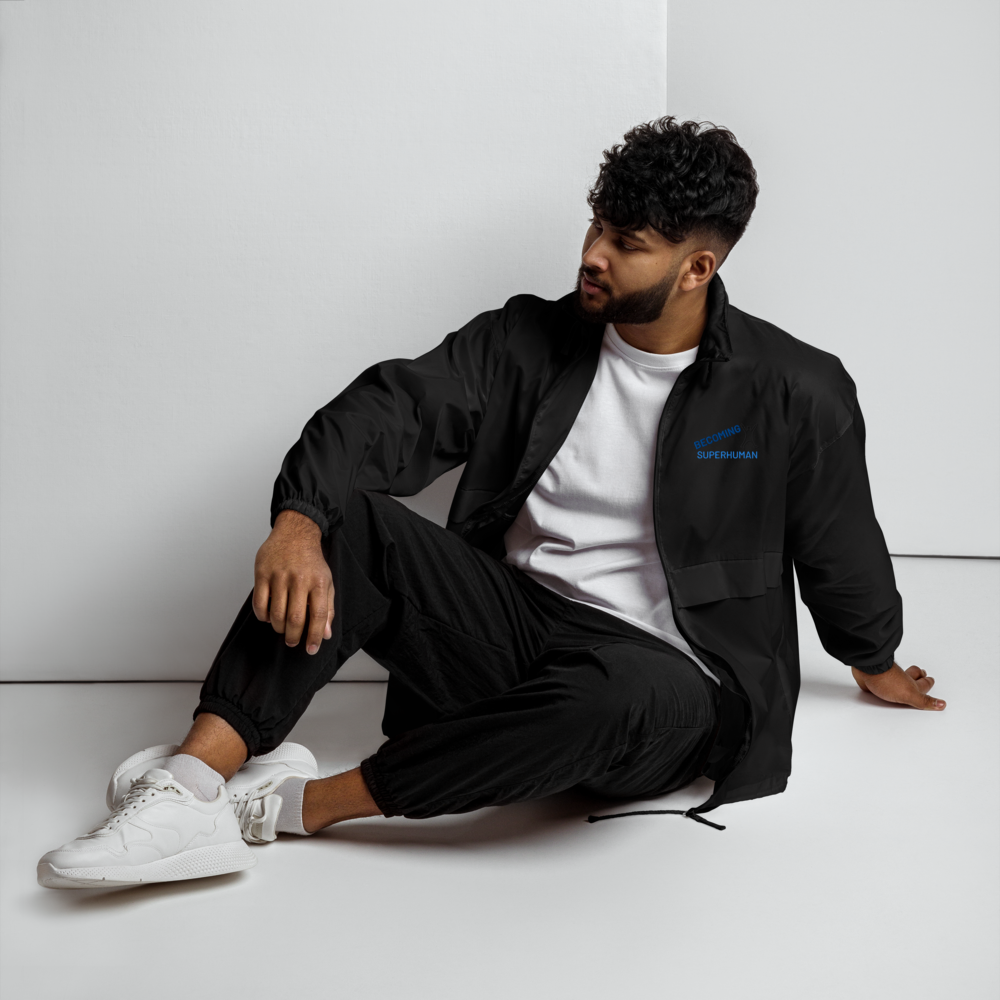 Hombre sentado usando el Cortavientos Negro Unisex VOOM — The Motion Code con texto azul en el pecho y estilo casual
