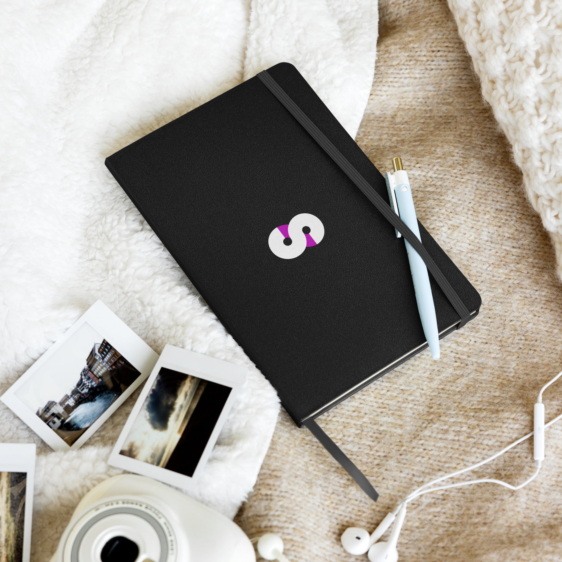 Cuaderno de Tapa Dura VOOM — The Archive Code sobre manta beige junto a fotos instantáneas y bolígrafo celeste