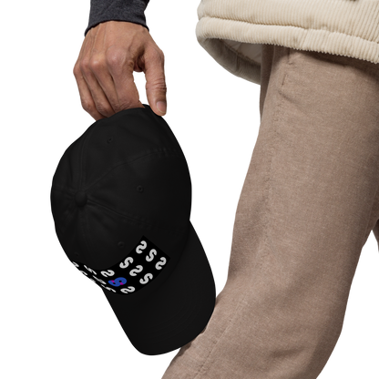 Persona sostiene la Gorra Negra VOOM — The Pattern Code mostrando detalle del símbolo azul y patrón repetitivo en visera curvada.